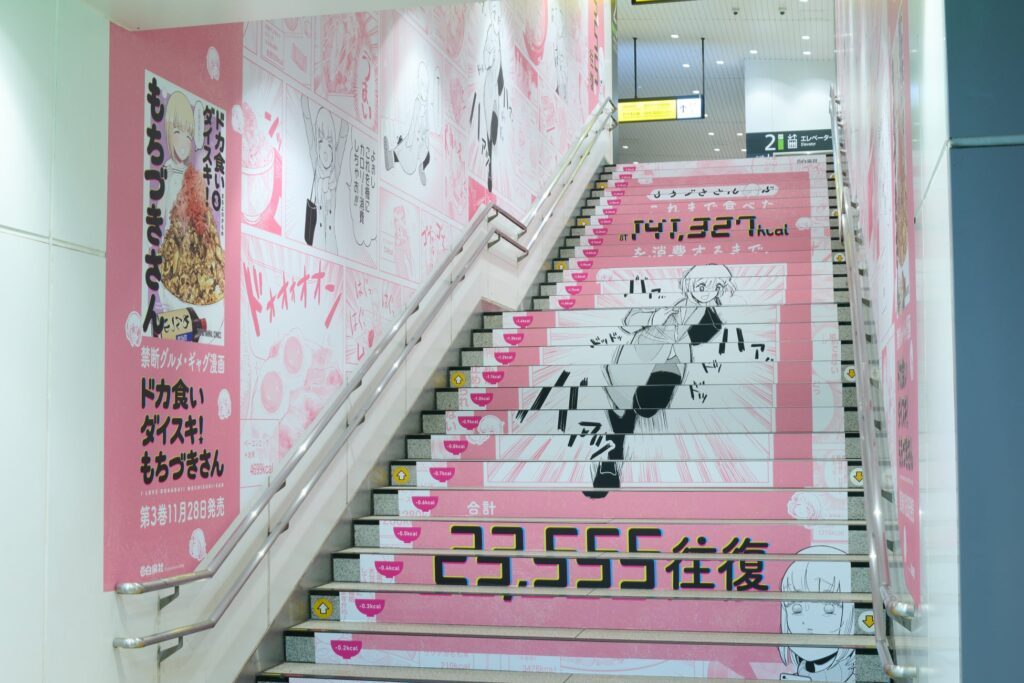 ドカ食い『もちづきさん』新刊発売で原宿駅にカロリー消費広告　階段を2.3万往復すればプラマイゼロ